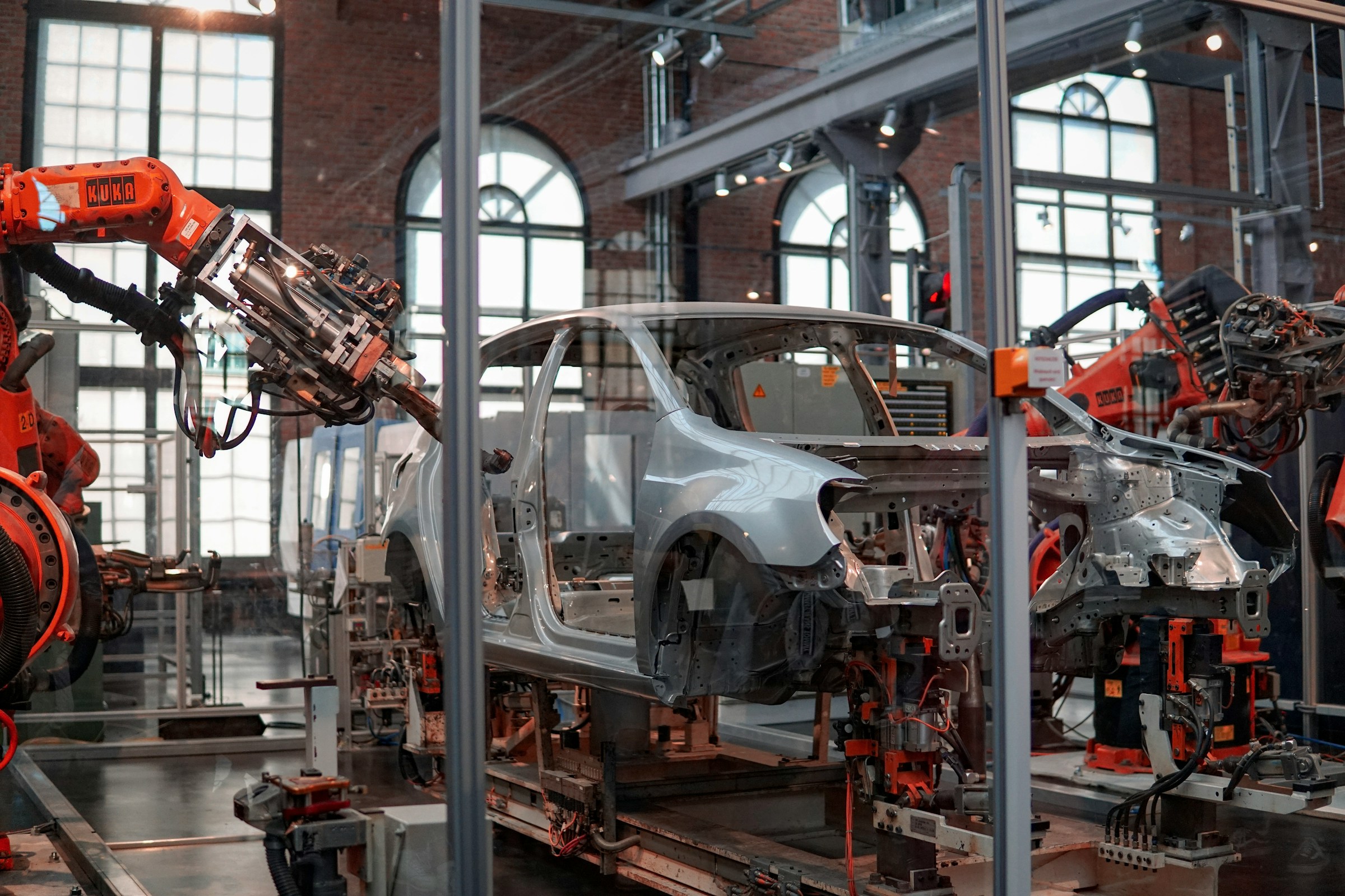 Grey vehicle being assembled by robotic machinery inside a factory